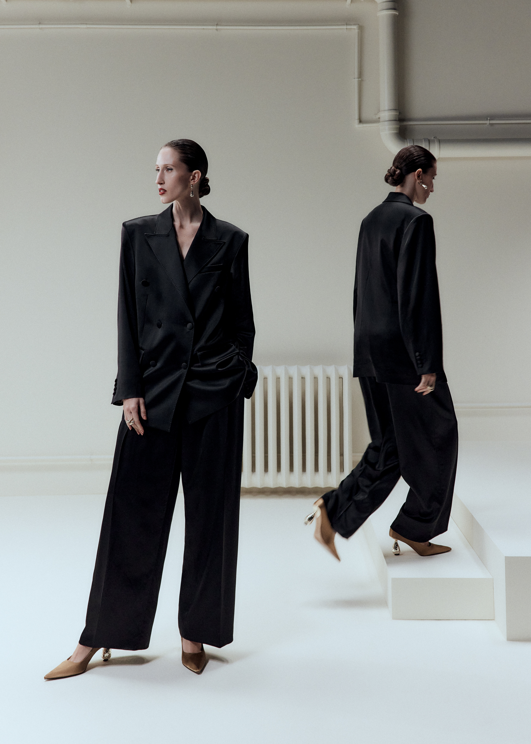 Two women wearing black satin suits and heels