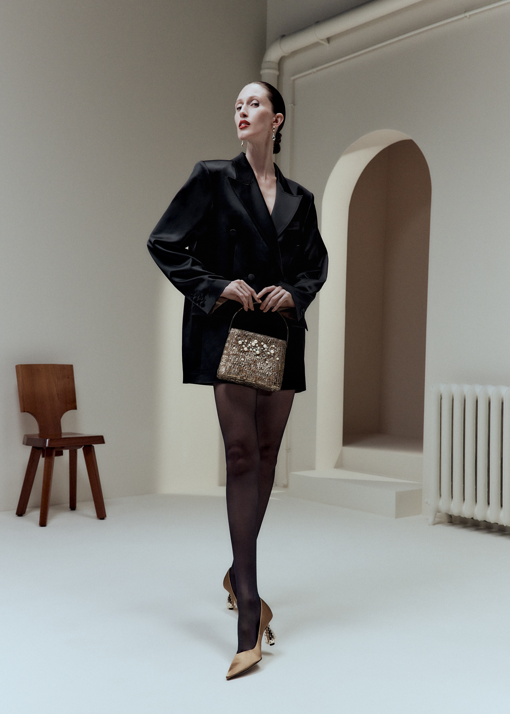 Woman in blazer and tights holding a gold clutch