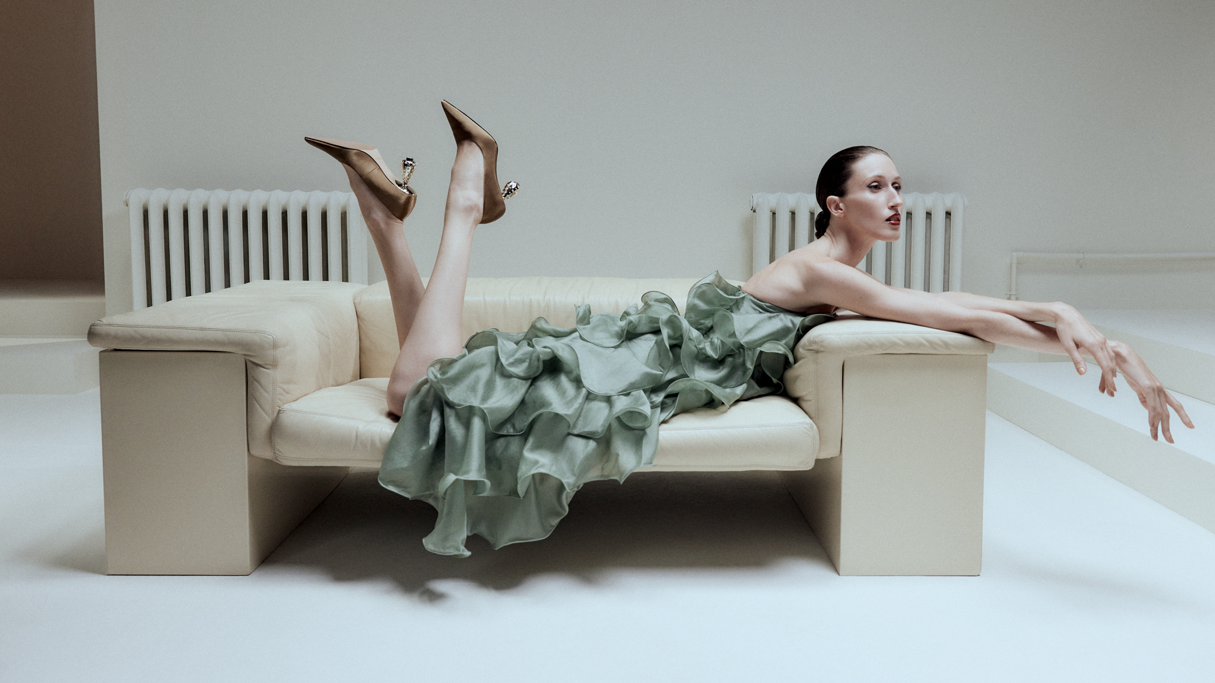 woman in green ruffle dress and heels laying on stomach on a couch