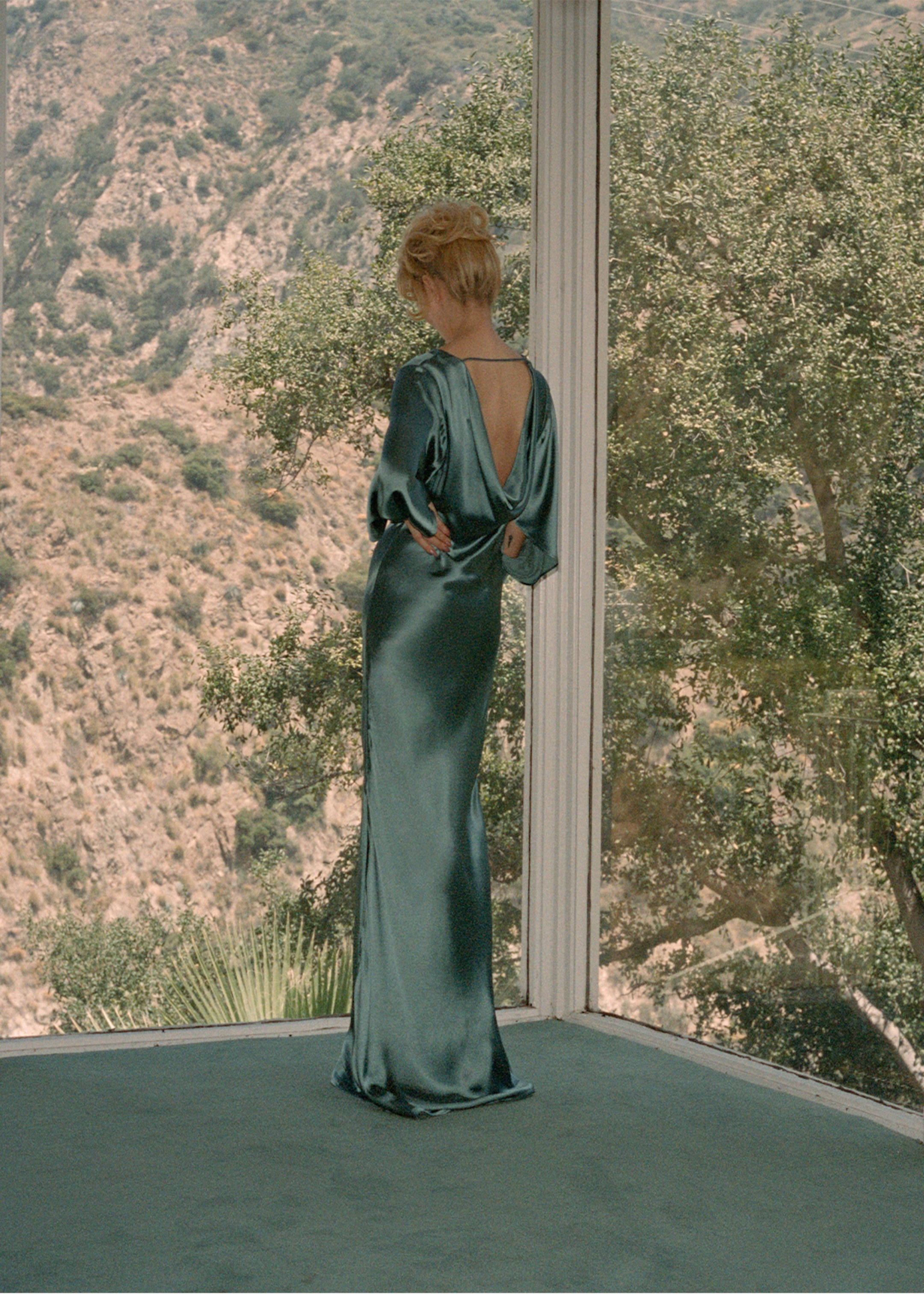 Woman standing by window in green long dress