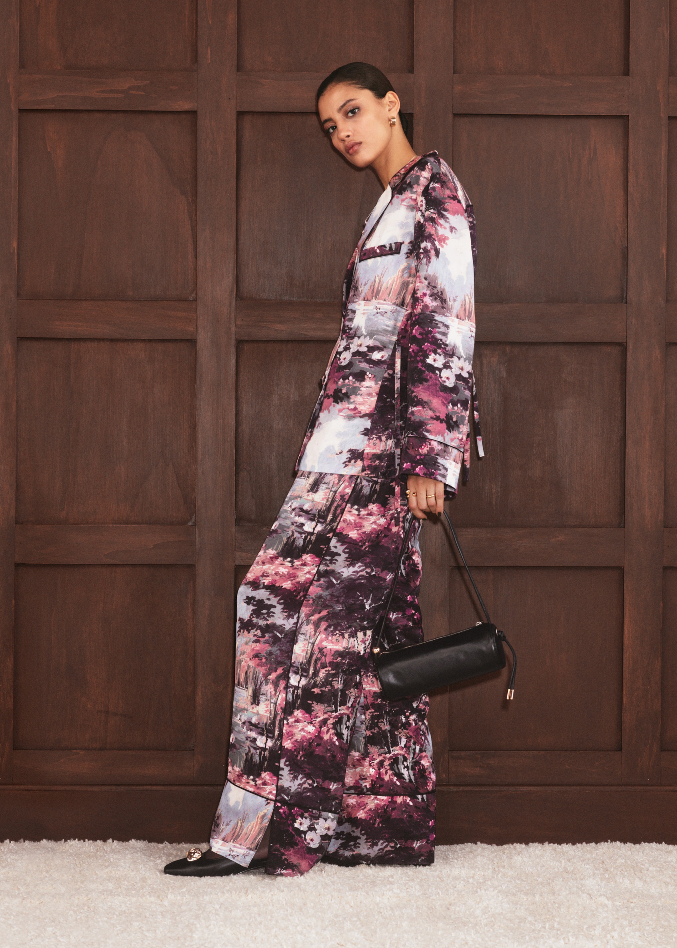 woman in patterned suit standing to the side holding a leather bag